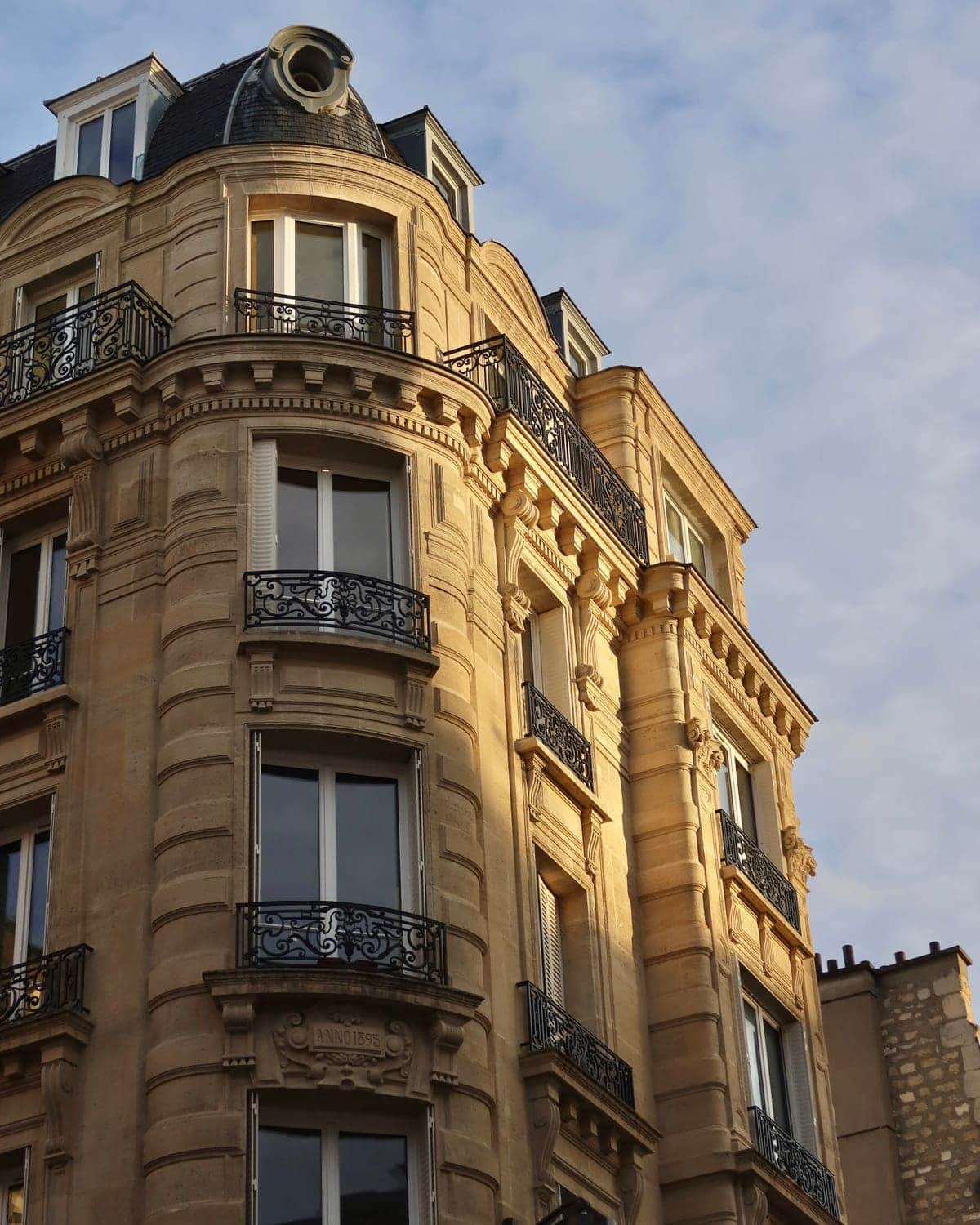 Façade d'angle d'un immeuble haussmannien en pierre de taille, balcons de fonte et toit de zinc à lucarnes, Paris