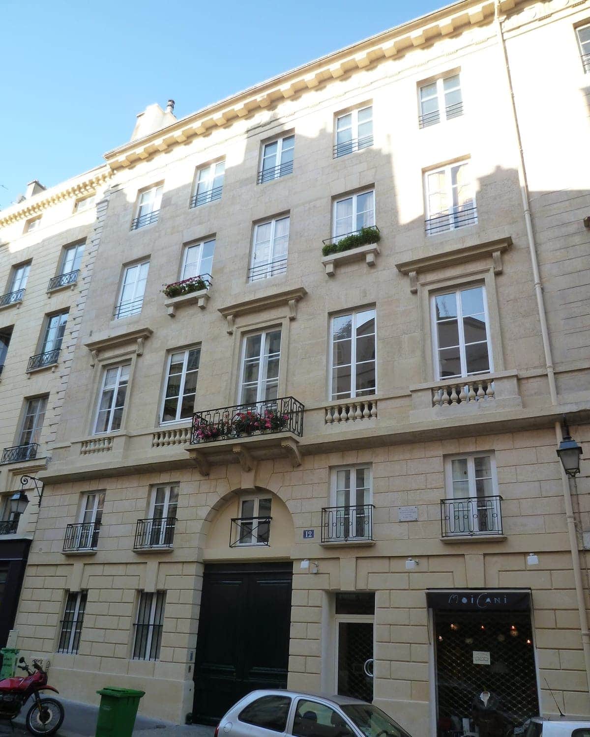 Façade en pierre rue de l'Odéon, porte cochère en bois sombre sous arcade et balcon fleuri, Paris